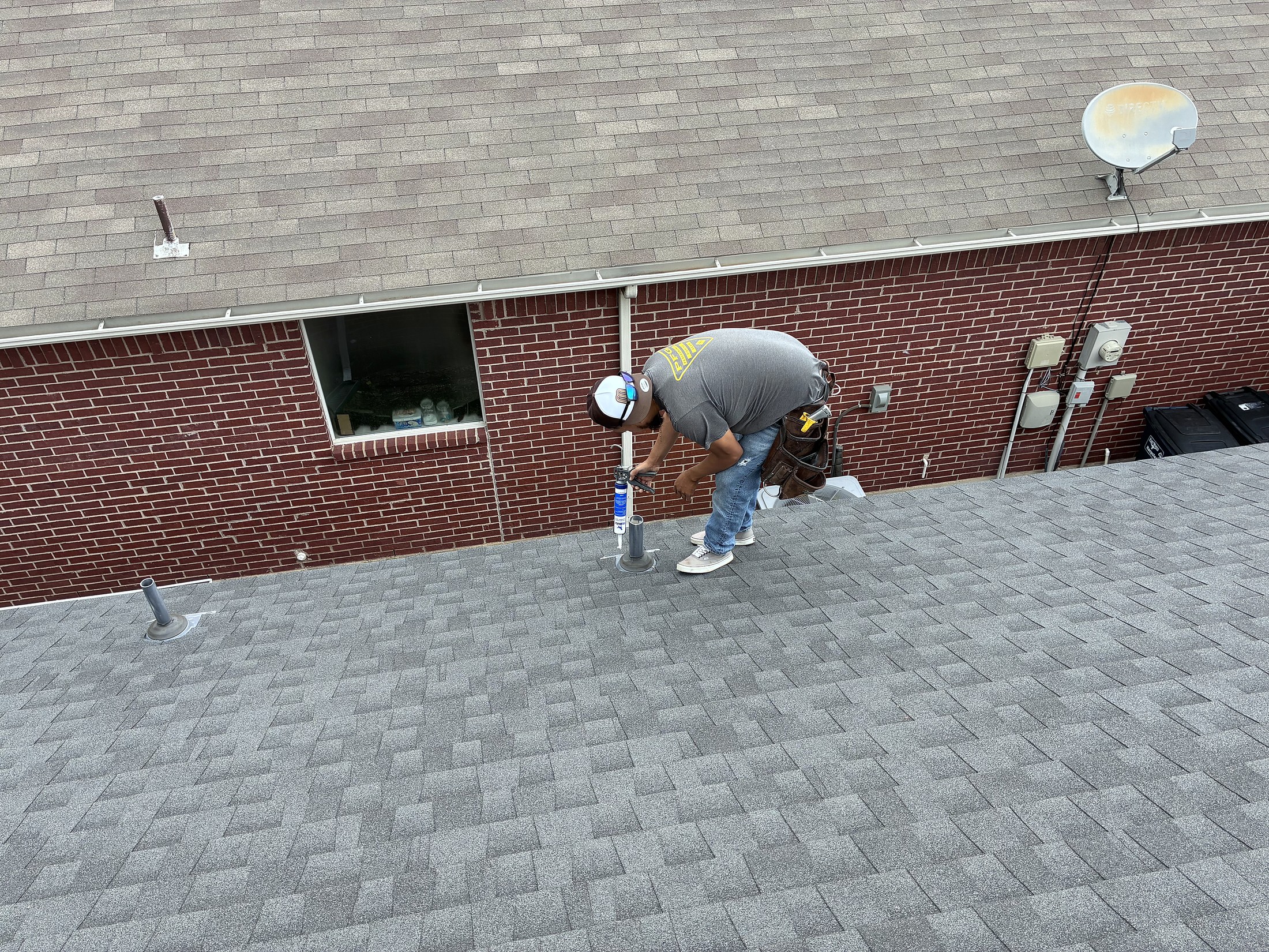 A worker sealing along a brick wall on a newly shingled roof