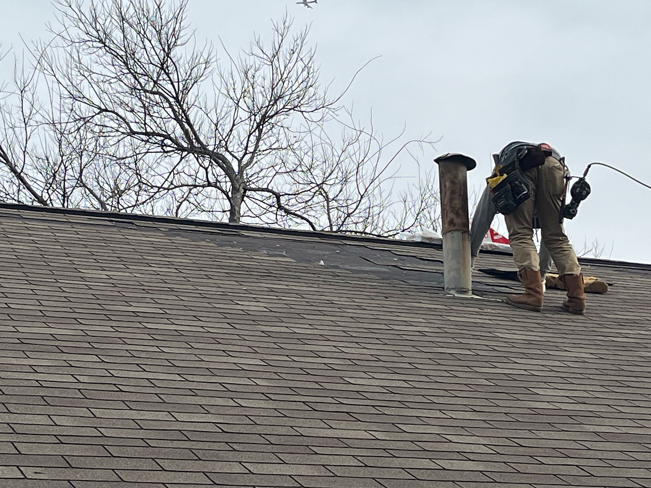 A roofer working at the vent stacks on a shingle roof