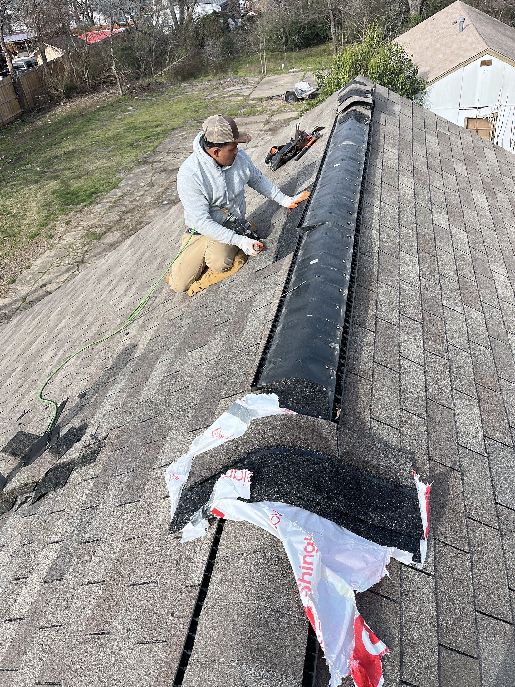 A worker setting ridge cap shingles along the ridge