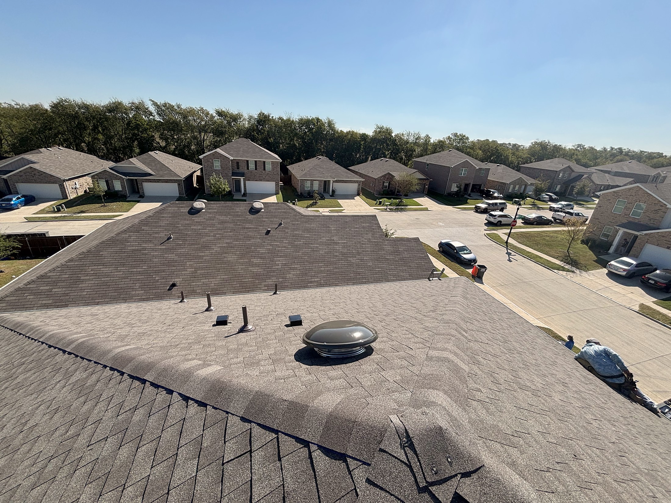 A low-slope roof section with a turbine vent, looking down a subdivision street