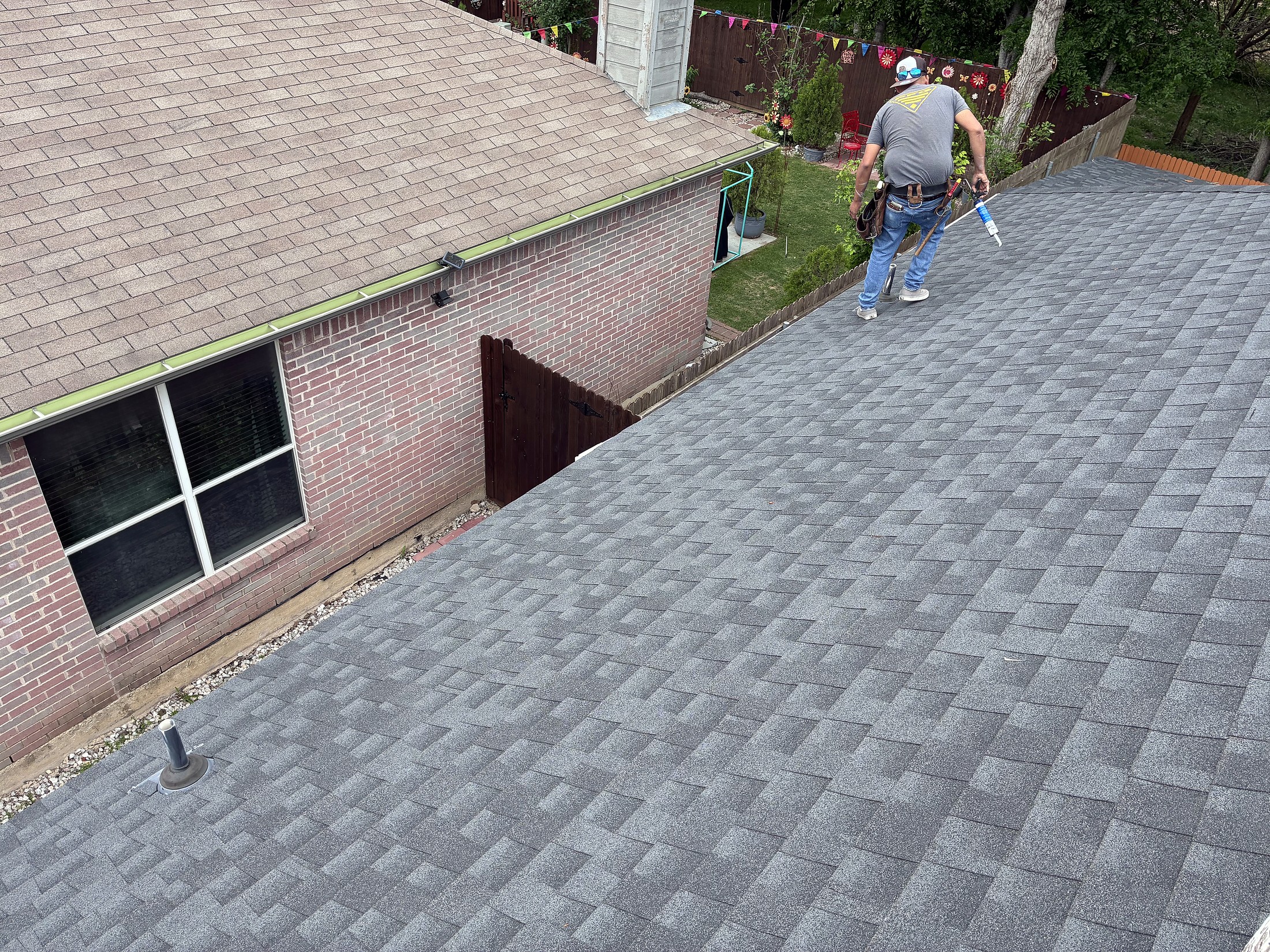 A worker walking across a newly shingled roof beside a brick wall
