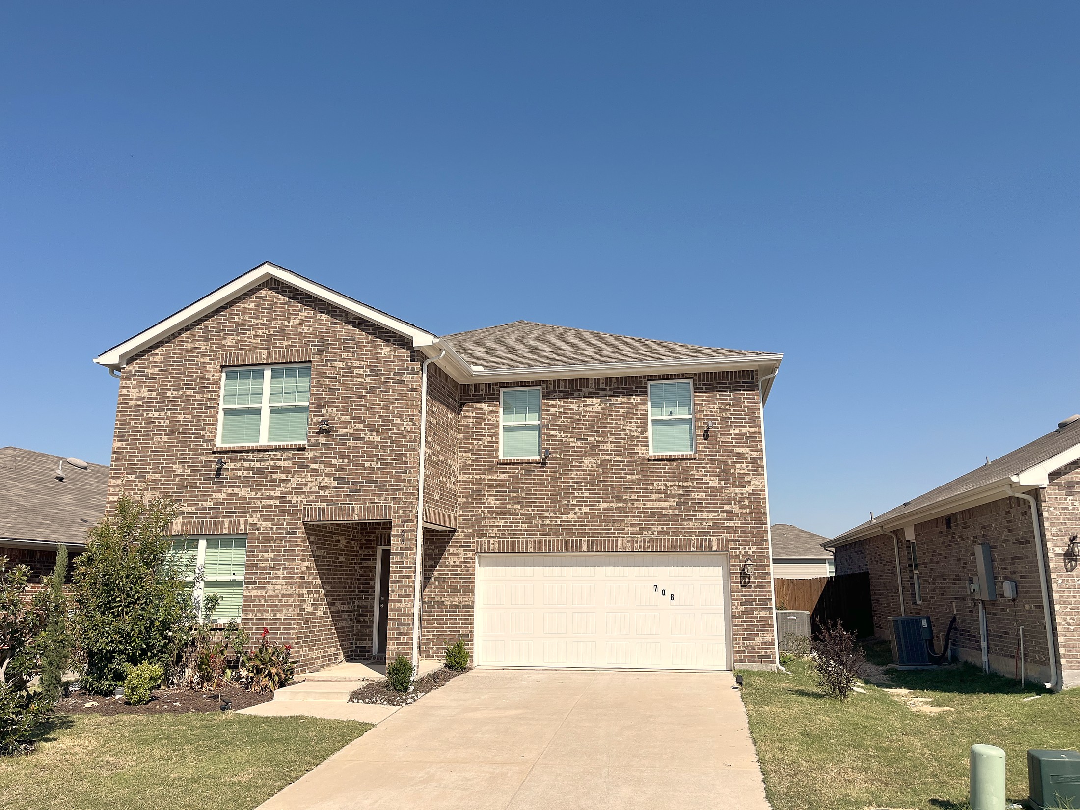 A two-story brick home with a finished roof under a clear blue sky