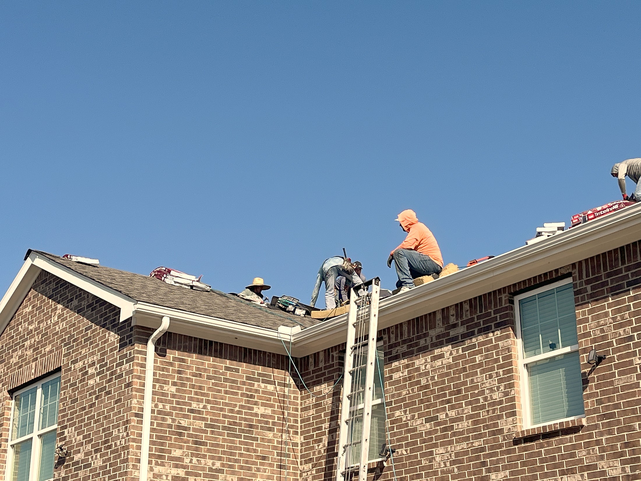 Crew members working along the eave of a brick home with a ladder set against it