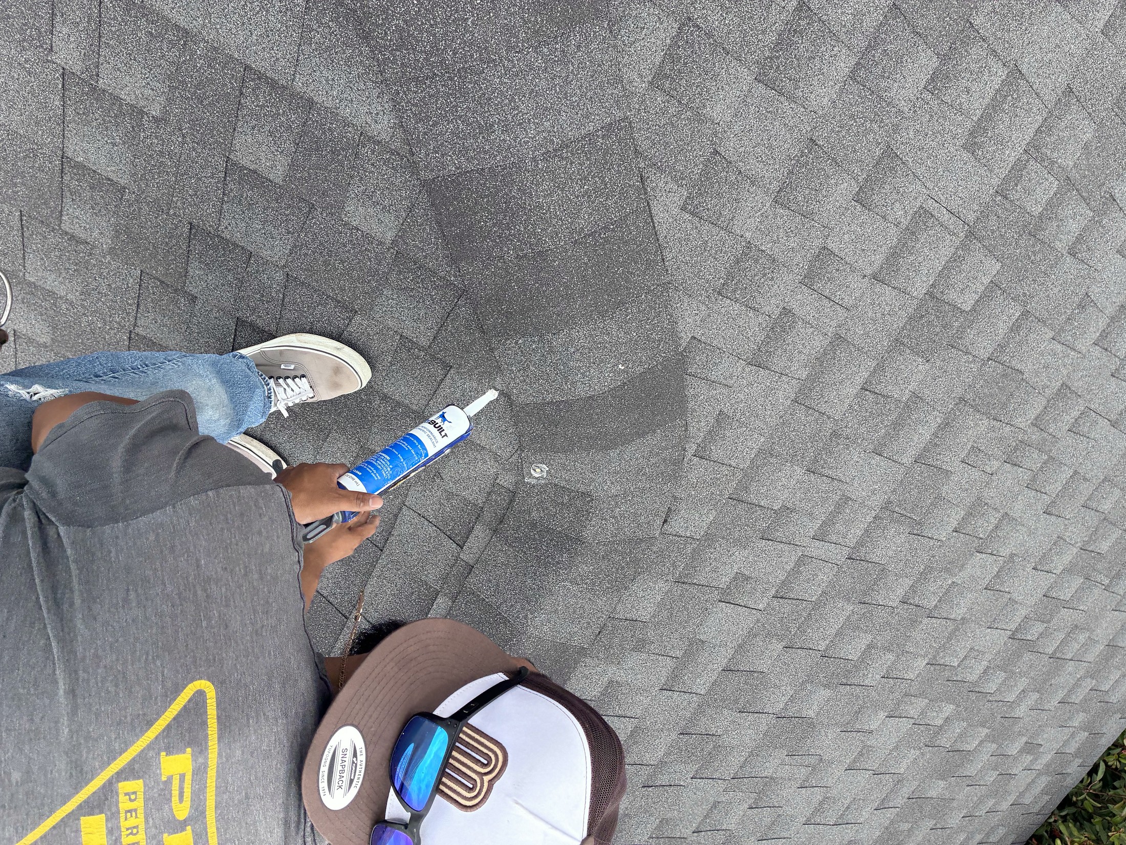 A roofer applying sealant on a shingle roof, seen from above