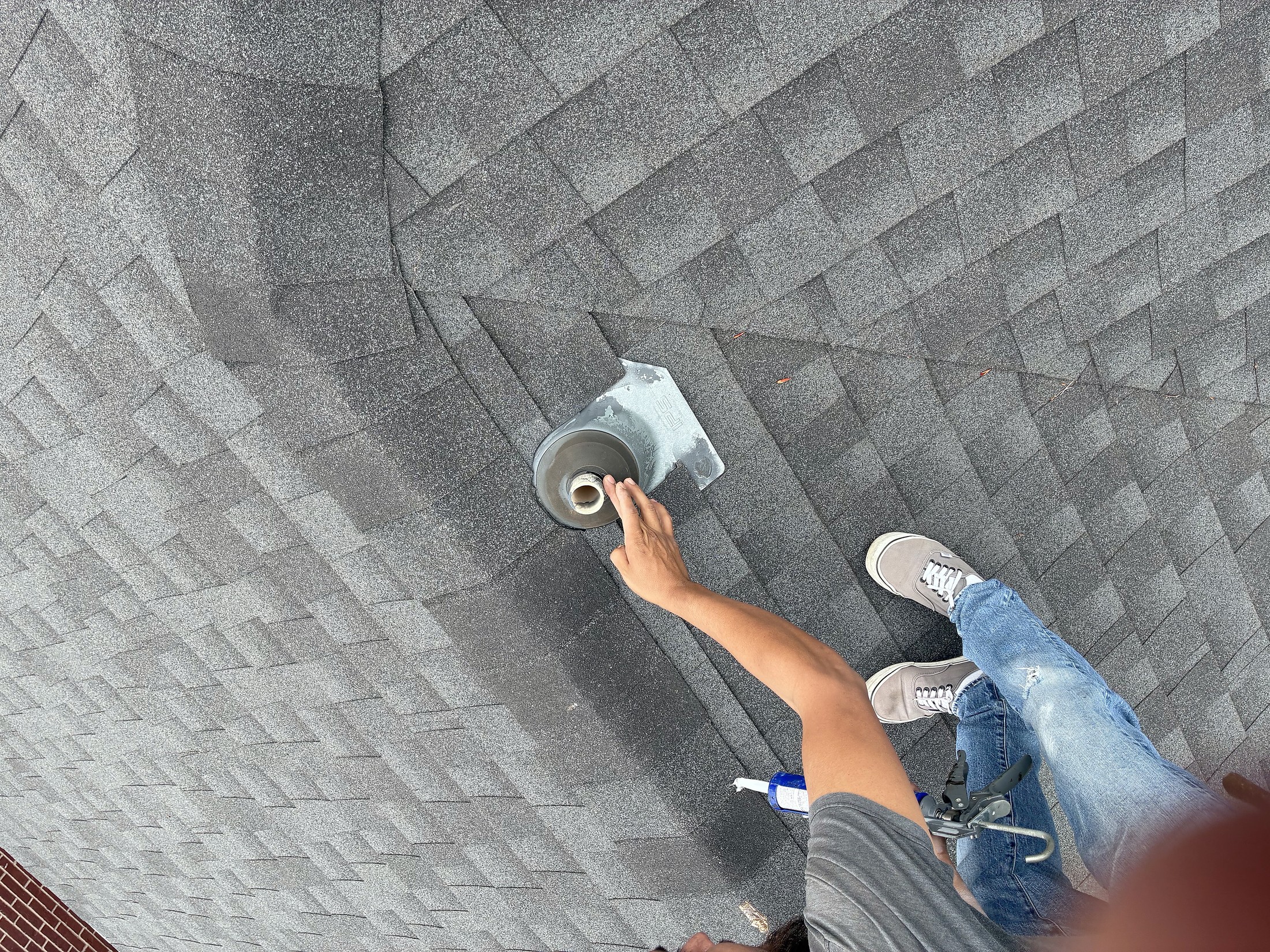 Hands sealing a fixing on a grey shingle roof